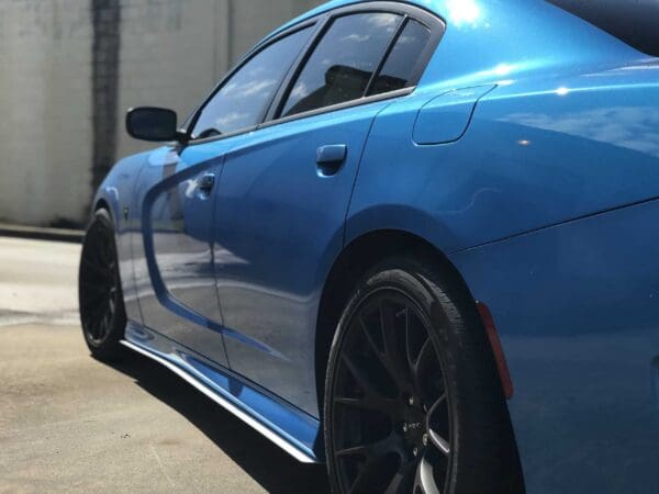 A blue sports car with black rims parked in a parking lot, reflecting sunlight on its sleek body.