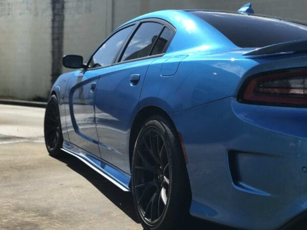 A blue sports car with tinted windows and black wheels parked in a sunlit parking lot.