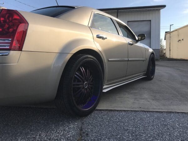 A silver car with custom wheels parked in front of a building with a garage door.