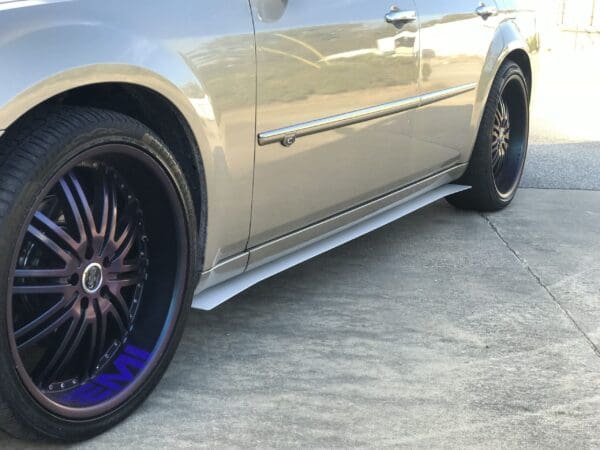 A silver car with custom rims parked in a driveway next to a building.