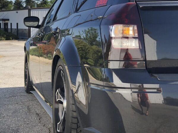 Close-up of a car's rear end, highlighting the taillight and reflections on the shiny black surface.