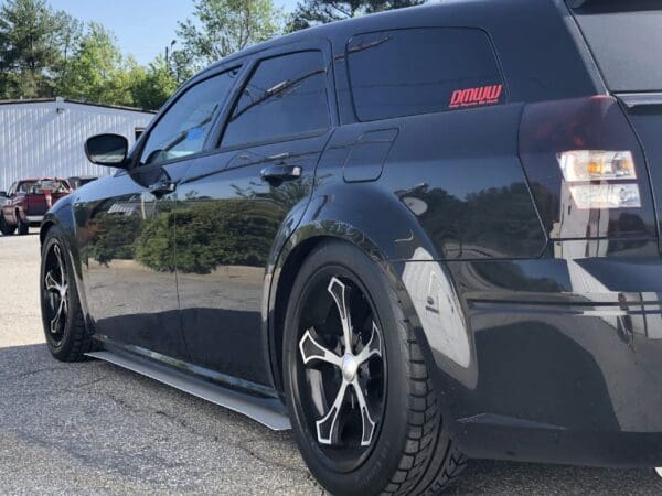 A black truck with a "DMWMW" decal on the window is parked in a parking lot on a sunny day.