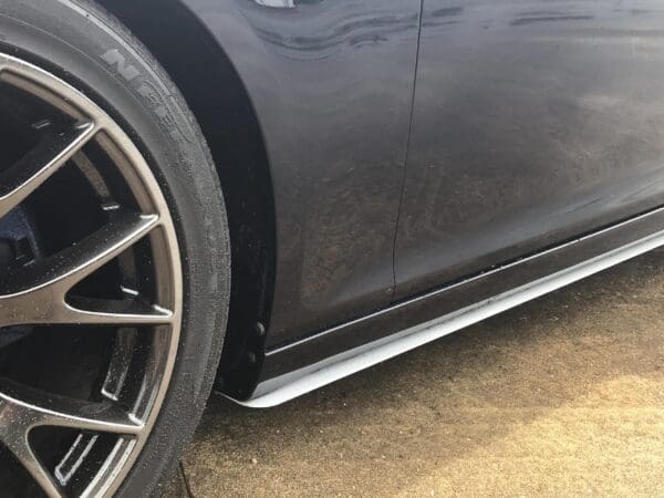 Close-up of a car tire on a street, showcasing the wheel rim and part of the vehicle's sleek black body.