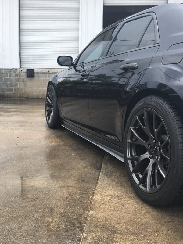 A sleek black car with stylish wheels parked in front of a white garage with closed shutters.