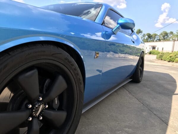 A blue sports car with black wheels is parked on the side of the road under a clear sky.