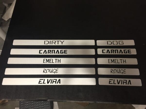 Metal pieces with cutout words: DIRTY, DOG, CARNAGE, EMELTH, ROUGE, ELVIRA, arranged in two columns on a black background.