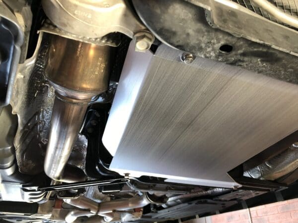 Close-up of a car's exhaust system, showing the catalytic converter and protective shielding underneath the vehicle.