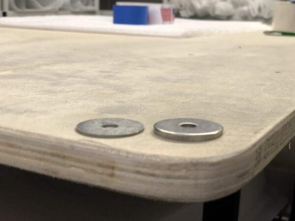 Two metal washers on a wooden surface, with blurred tools and materials in the background.
