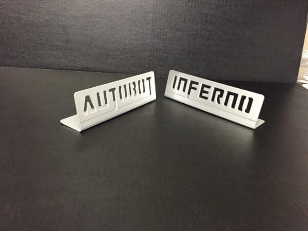 Two metal pieces displaying the words "AUTOBOT" and "INFERNO" against a dark background.