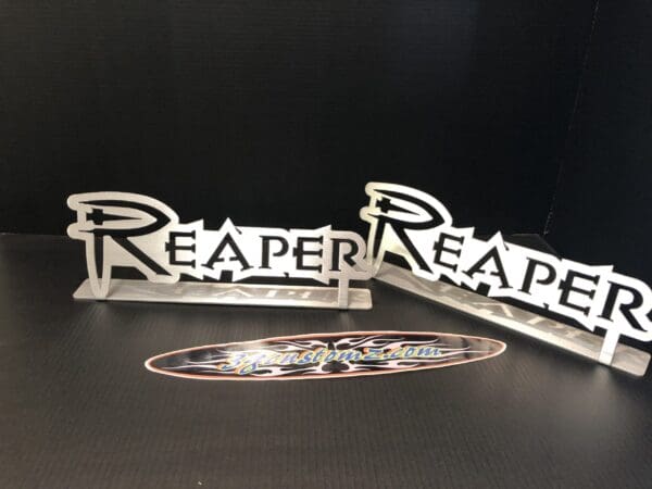 Two metal signs with the word 'REAPER' on a table, with a logo sticker reading '3gcustomz.com' below.