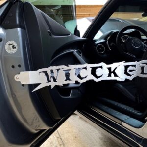 A car door is open, displaying a "WICKED" sign attached to the door frame. The interior is visible.