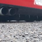 Close-up of a red car's rear diffuser and dual exhaust pipes on a gravel surface.