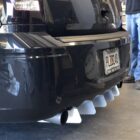 Black car rear with a custom diffuser and dual exhaust pipes; a person stands nearby.