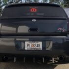 Black car rear view with a prominent rear diffuser, custom license plate, and decals on the rear window.
