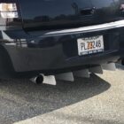 Black car rear featuring dual exhaust pipes and a silver rear diffuser. License plate visible.