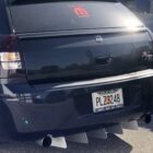 Black car with a rear diffuser, custom license plate, and stickers on the back window.