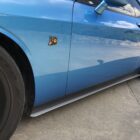 Blue car with black wheels, showing a side view and a decorative emblem on the door.