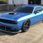 A blue Dodge Challenger with a hood scoop and black wheels parked on a concrete surface.