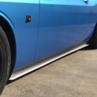Close-up of a blue car's side, featuring a black wheel and a decorative emblem.