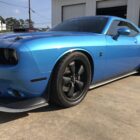 A blue sports car with black wheels parked on a concrete surface, showcasing its sleek design and aggressive stance.
