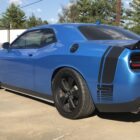 A blue sports car with black accents parked on a concrete surface, surrounded by trees and buildings.