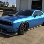 A blue muscle car with a hood scoop and black wheels parked on a concrete surface.