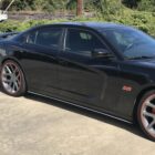 Black sedan with large silver wheels and red accents parked on a concrete surface.