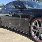 Black car with large silver wheels and red accents parked on a concrete surface.