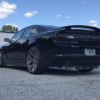 Black Dodge Charger parked on asphalt, showcasing custom wheels and rear design against a cloudy sky.