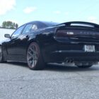 Black Dodge Charger parked on asphalt, showcasing large wheels with red accents and a sporty rear design.