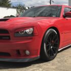 A red Dodge Charger SRT8 parked on a concrete surface, showcasing its sleek design and black wheels.