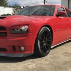 Red Dodge Charger SRT with black rims parked on concrete, showcasing a sporty design and aggressive stance.