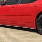 Red car with black rims parked on a concrete surface, showcasing a side view and custom side skirt.
