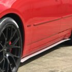 Close-up of a red car's side, featuring black alloy wheels and a HEMI badge.