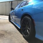 A blue car with black wheels parked on a concrete surface, showing its side profile.