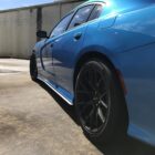 A blue car with black rims parked on a concrete surface, showing its side profile and sleek design.