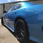 A blue car with black rims parked on a concrete surface, reflecting sunlight and nearby structures.