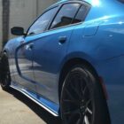 A blue car with black rims parked on a concrete surface, reflecting sunlight.