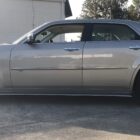 A silver sedan parked on a concrete surface, showcasing its side profile and dark wheels.