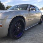 A silver sedan with custom black and purple rims parked on a concrete surface under a clear sky.