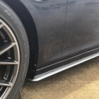 Close-up of a car's wheel and side skirt, showcasing a sleek design and wet surface.