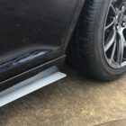 Close-up of a car's side with a silver side splitter and a black tire on a wet surface.