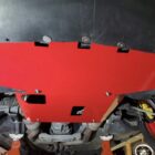 Red skid plate mounted under a car, showing bolts and surrounding mechanical components.