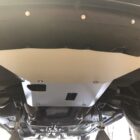 A metal skid plate is mounted under a vehicle, showing bolts and surrounding components.