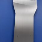 Metal transmission cover plate with a sloped design, mounted against a blue background.