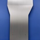 Metal transmission cover plate with a tapered top and multiple mounting holes, set against a blue background.