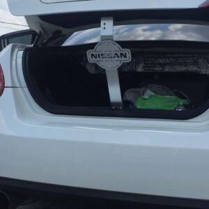 Open trunk of a white Nissan car, displaying a towel and a spray can inside.