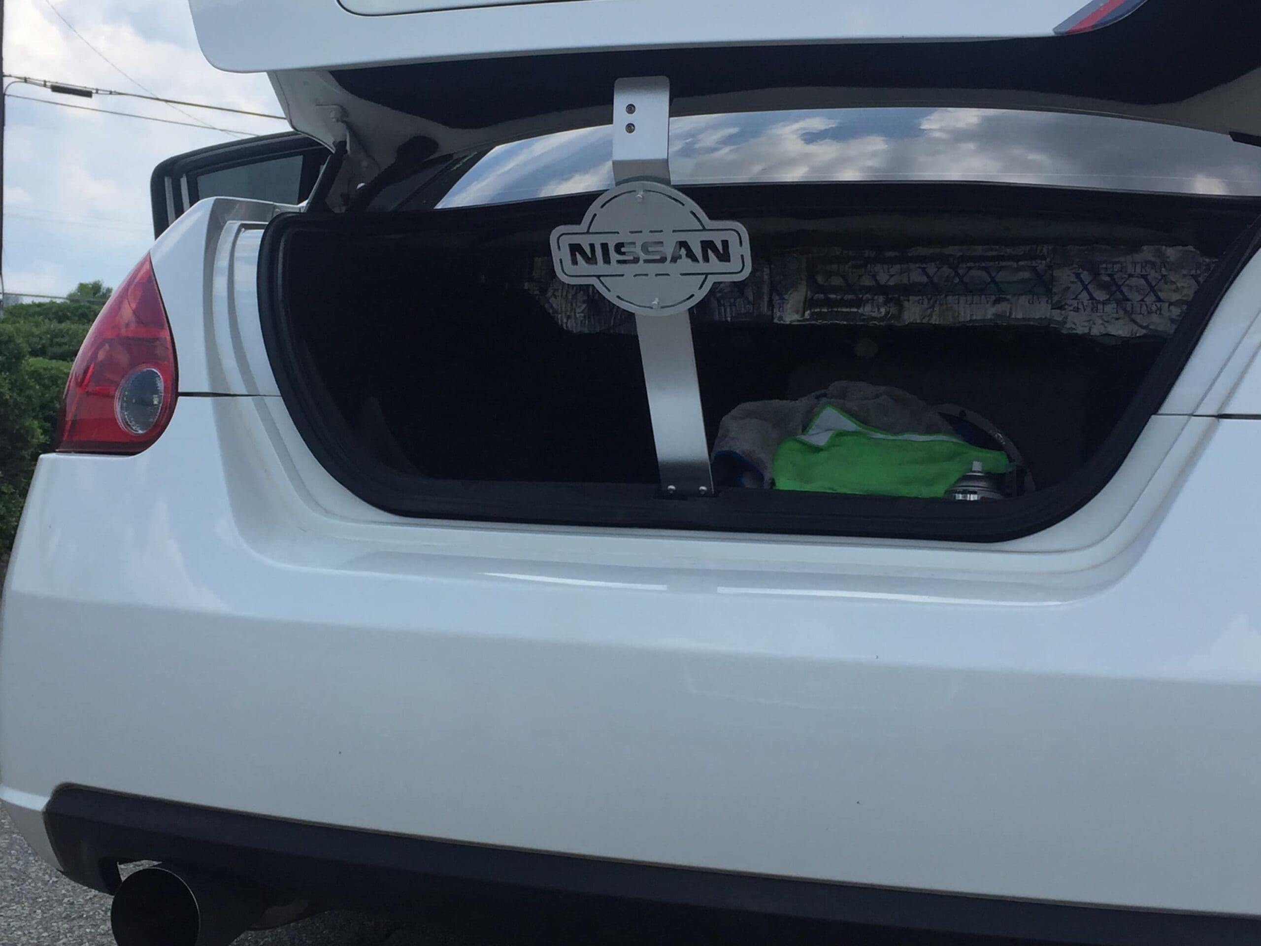 Open trunk of a white Nissan car, displaying a towel and a spray can inside.