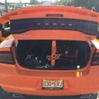 Open trunk of an orange Dodge Charger, revealing bags and a decorative strap.