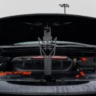 Car trunk open, showcasing engine components and a decorative metal piece with a stylized face.